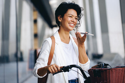 Smiling woman sending a voice memo while holding bicycle in urban city environment