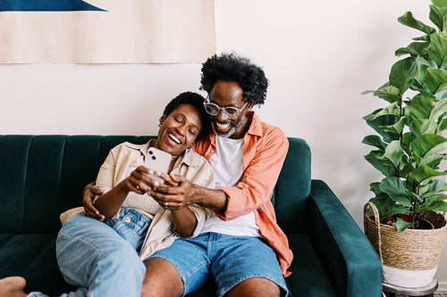 Couple relaxing together in living room, connecting through video chat on smartphone