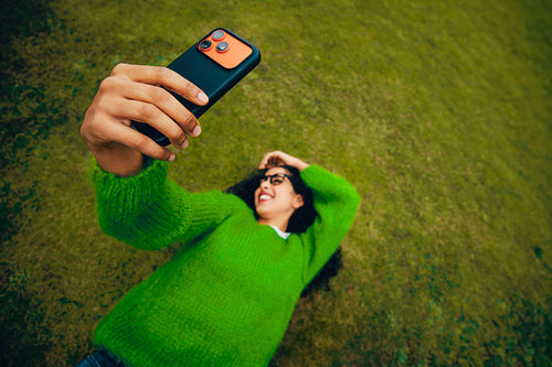 Smiling woman takes a selfie with a smartphone while lying on grass outdoors