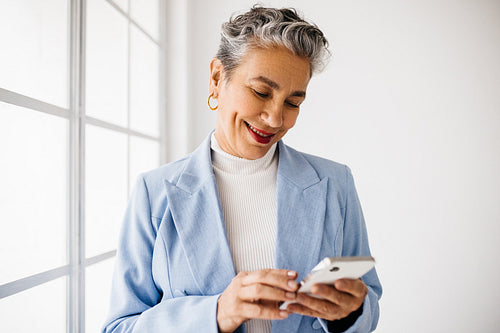 Mature business woman smiling as she reads a text message in her office