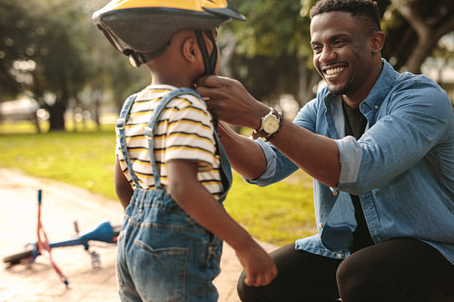 Man helping son wearing helmet for cycling at park