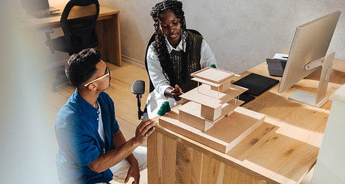 Two young architects discussing a building model in a modern office workspace.