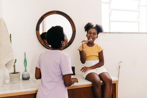 Morning oral hygiene: Little girl brushing her teeth with her mom in the bathroom