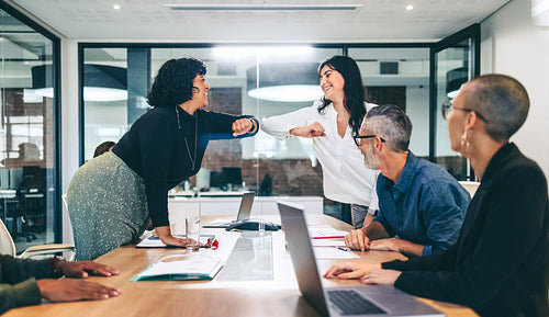 Two cheerful businesswomen elbow bumping each other before a meeting