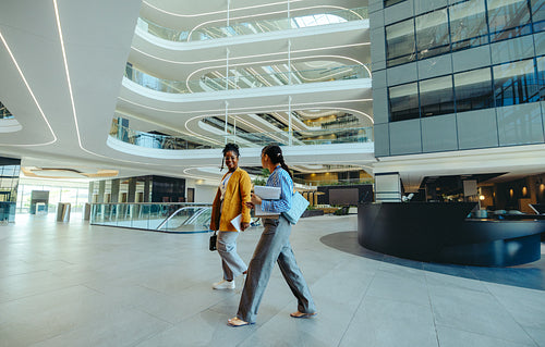 Two female corporate professionals walking in modern office lobby