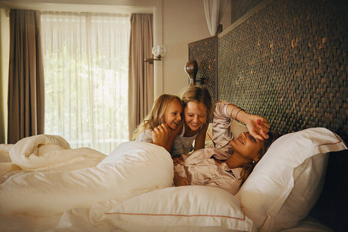 Happy family waking up together in a cozy hotel room bed on a sunny morning