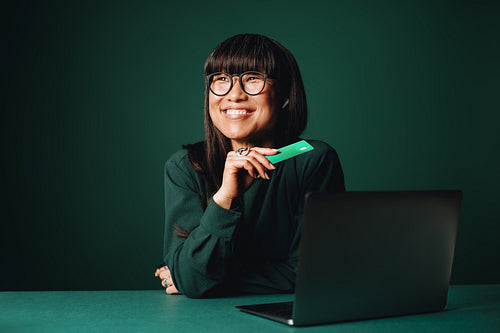 Woman using laptop and credit card for online payment in monochromatic studio setting