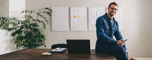 Successful businessman smiling at the camera while holding a smartphone