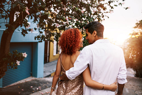 Rear view of a romantic couple walking on street at sunset.