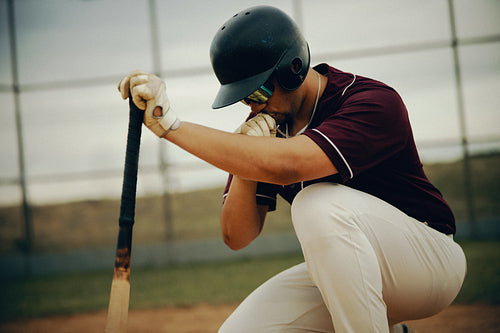 Baseball player kneeling with bat in a pre-game ritual for good luck on the field