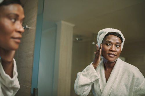 Mature woman in bathrobe putting on cream on her face skin