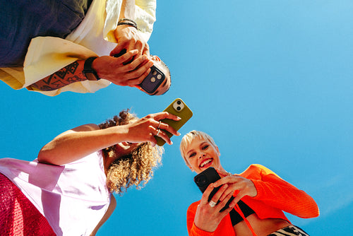 Friends use smartphone together outdoors against a clear blue sky