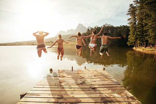 Young people jumping from pier into lake together