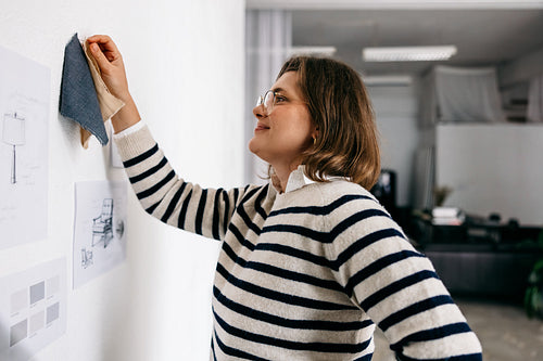 Furniture designer woman planning material selection with fabric samples and sketches on studio wall