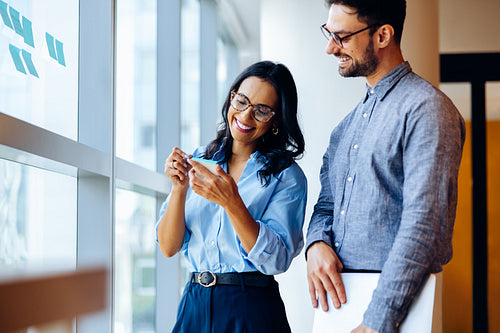 Smiling colleagues discussing a project while looking at a notepad by a window