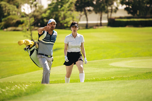 Man carrying golf bag and talking to female golfer on the golf course