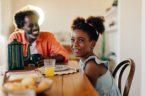Happy black girl enjoying a pão de queijo breakfast with her dad at home