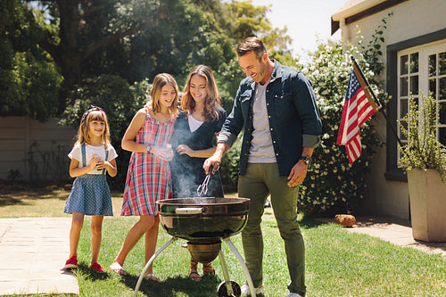 Couple standing with their kids in their backyard making barbeque