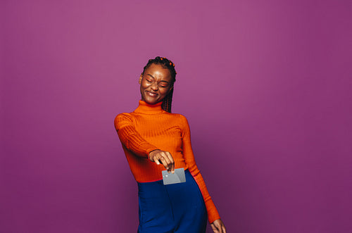 Cheerful african woman paying with contactless card on vibrant purple background
