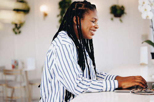 Happy young business woman typing on a laptop while working in a cafe