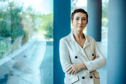 Confident professional woman standing by a glass window outdoors