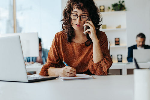 Professional business woman focused on writing, working at her laptop in creative startup office