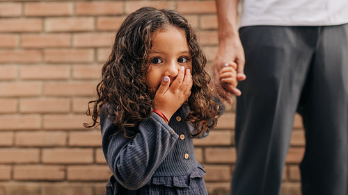 Cute little girl looking at the camera while holding her father's hand