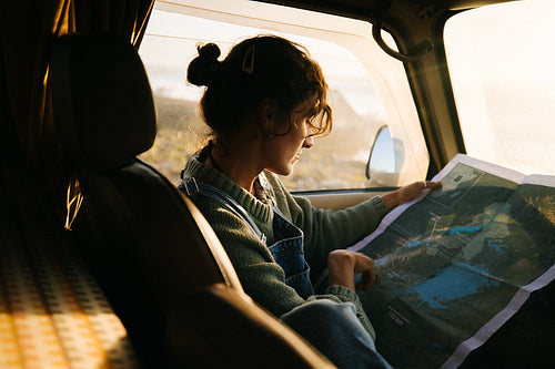 Woman studies map in car during sunset road trip