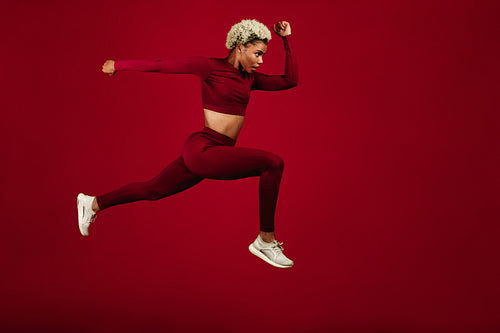 Female sprinter running on maroon background