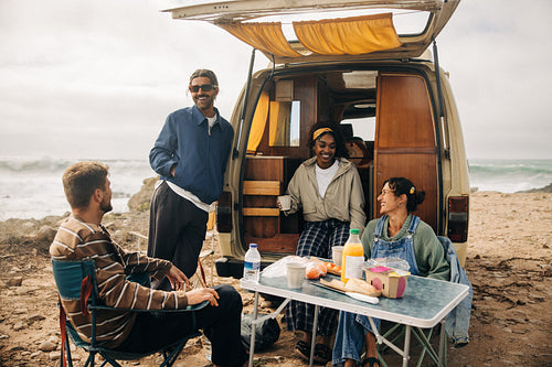 Friends share a beachside picnic beside a vintage van