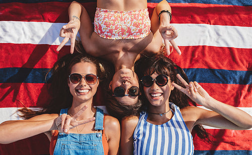Smiling female friends with peace sign lying at the beach