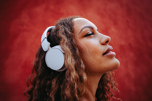 Woman enjoys immersive music with headphones against red wall