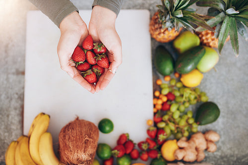 Woman holding a handful of fresh strawberries over chopping board
