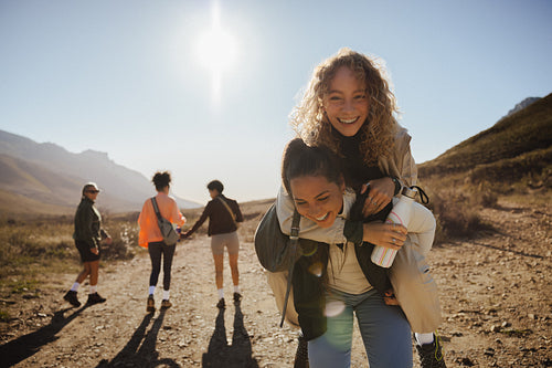 Friends laughing and piggybacking during sunny mountain hike