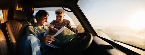 Couple in a camper van map reading at sunset during a road trip