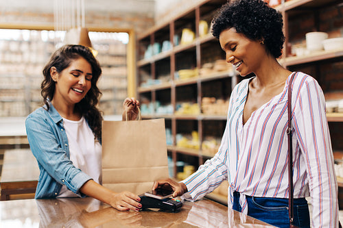 Cheerful female customer making an NFC payment in a ceramic store