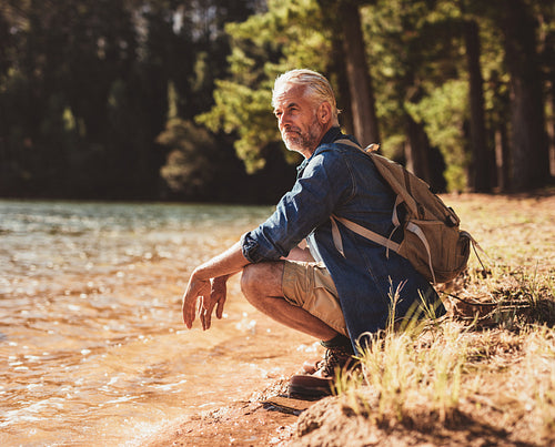 Mature man sitting next to a lake admiring the view