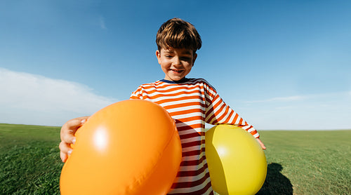 Boy with balloons in sunny field smiling