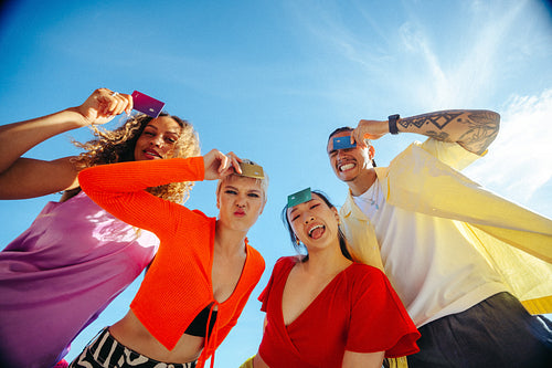 Young adult students hold payment cards overhead under a blue sky