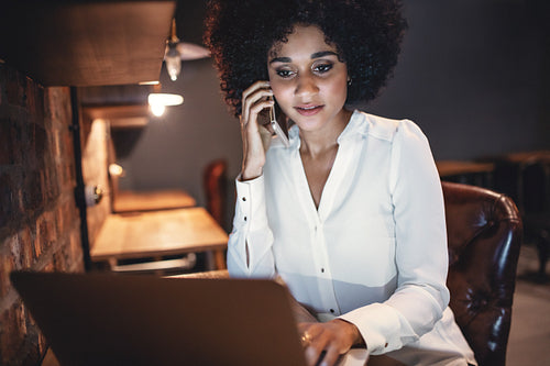 Businesswoman working on laptop and talking on mobile phone in cafe