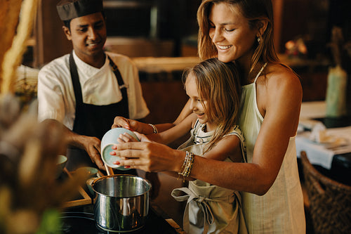 Mother and daughter enjoying cooking with a chef in a restaurant kitchen