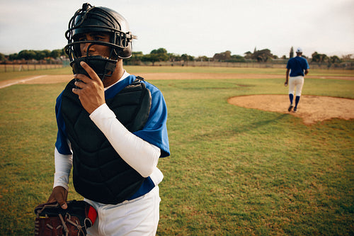 Baseball players on the field preparing for the game with one wearing catcher's gear