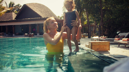 A happy mother playing and laughing with her young daughter in a tropical swimming pool