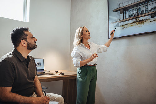 Young woman presenting architectural designs to middle-aged man in modern office setting