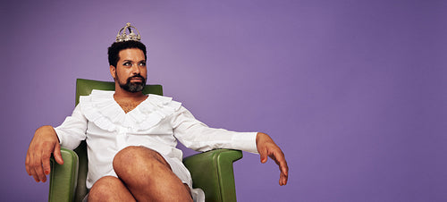 Attractive drag queen with crown sitting on his thrown