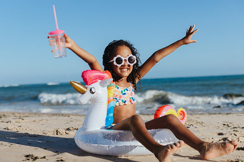Happy girl on beach with unicorn float and drink enjoying summer vacation