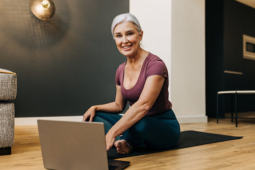 Virtual yoga: Woman exploring online yoga resources while sitting on her mat