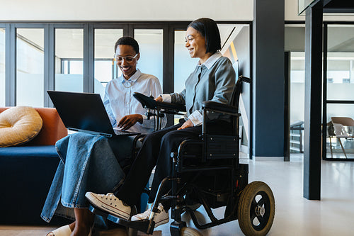 Professional workplace interaction between colleagues, one using a wheelchair, discussing ideas