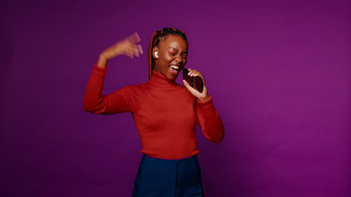 Energetic young woman sings and dances with smartphone microphone on purple background