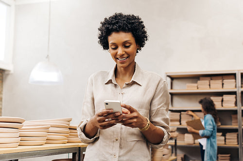 Happy female ceramist reading a text message on her smartphone